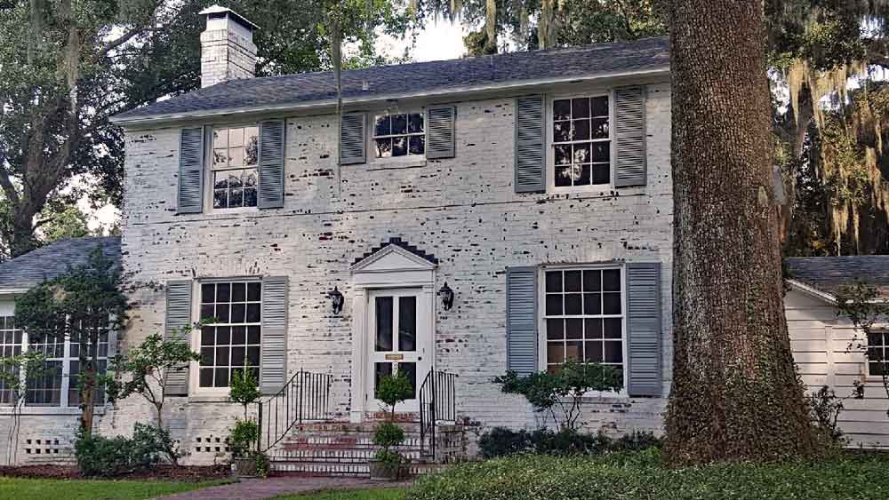 Exterior Southern shutters installed on the outside of a white brick house with Spanish moss.