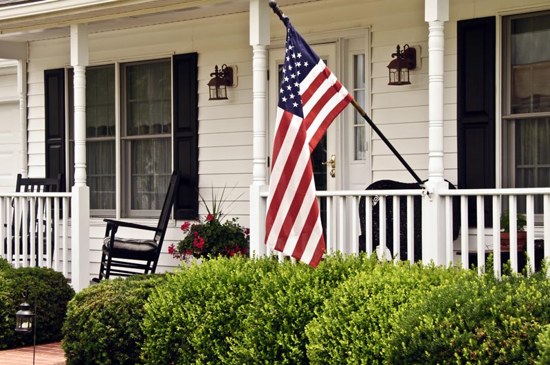 Black exterior American shutters on the porch with an American flag.