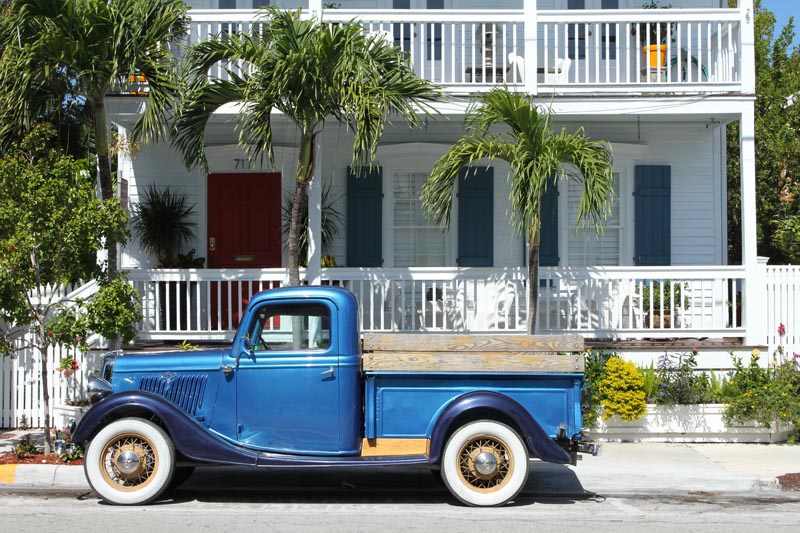 Florida Keys shutters installed on a white house with blue truck.