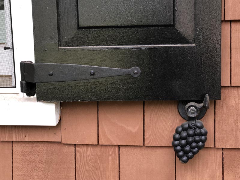 Iron grape shutter dog with hinges on a black exterior shutter.