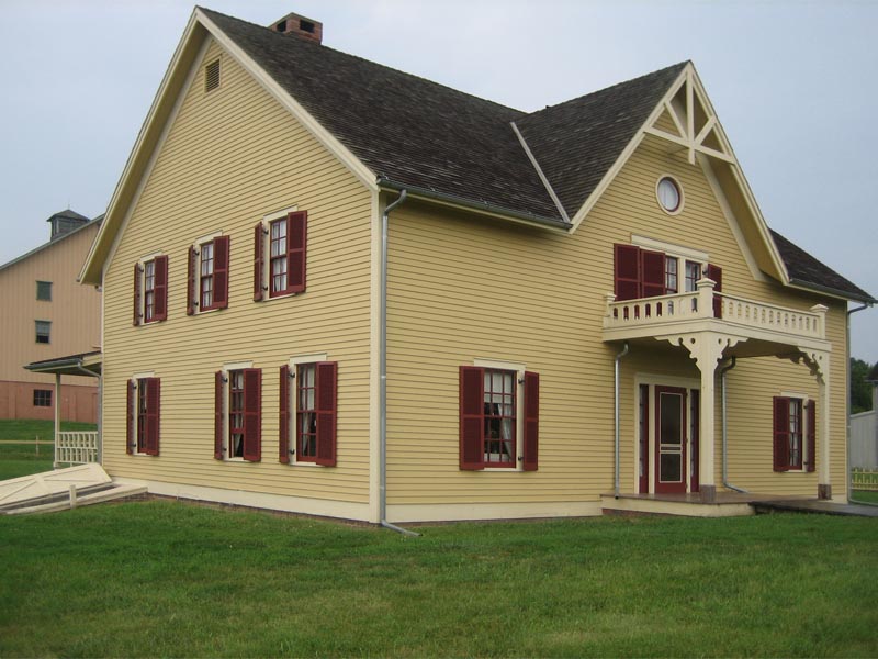 Yellow house on a traditional farm with red exterior shutters.