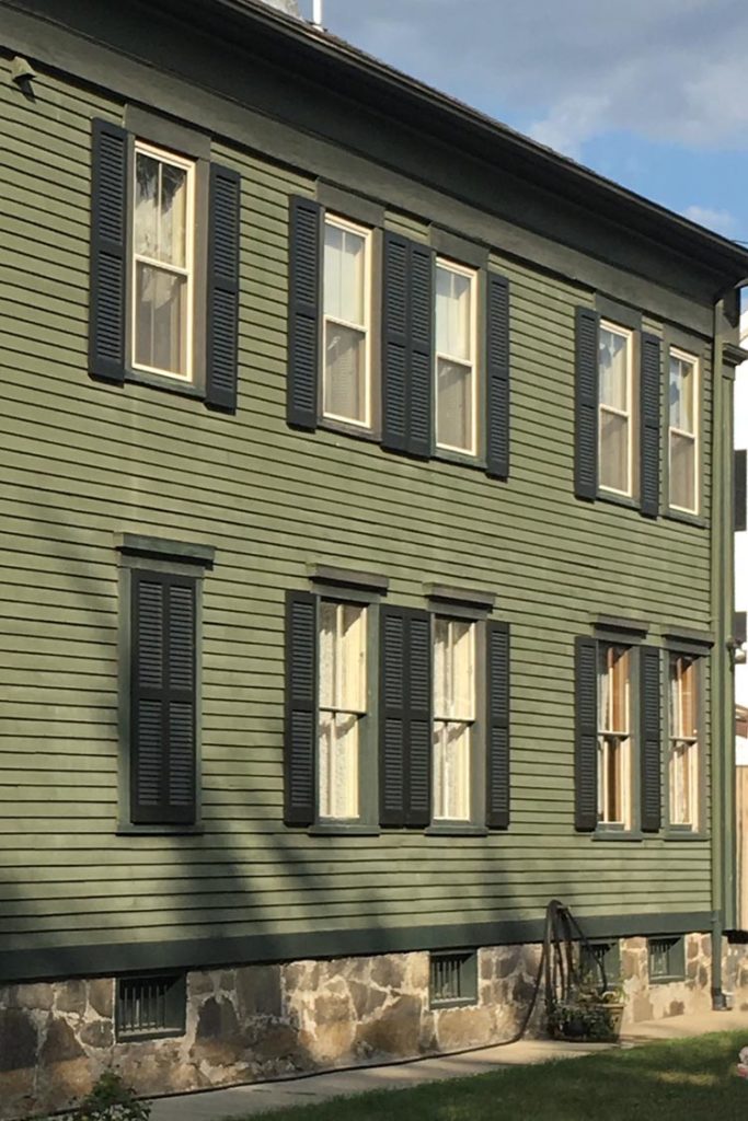 Dark green shutters installed on a house with green siding.