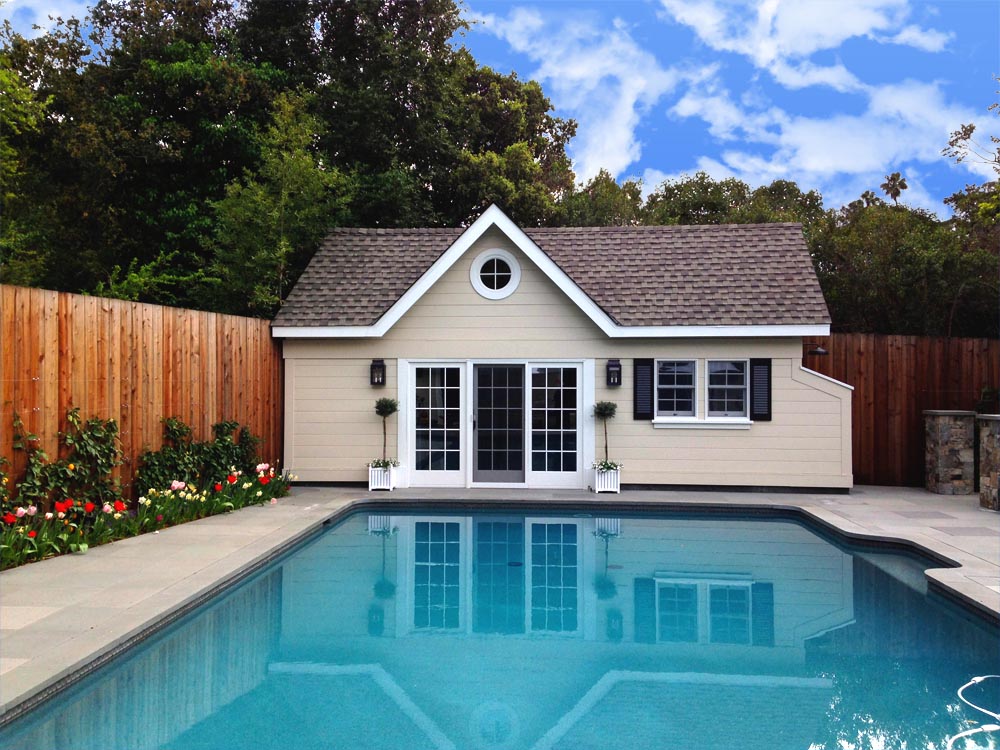 Pool house with fence, flowers, and louvered window shutters.