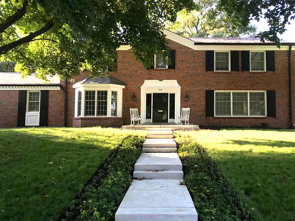 Brick house with exterior black shutters and white rocking chairs and trim.