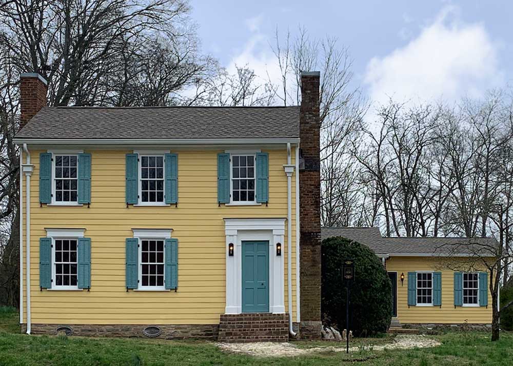 Yellow house with green front door and louvered exterior shutters.