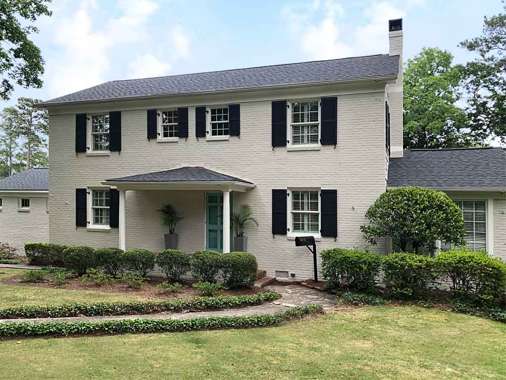 Exterior black shutters with slats installed on a white brick house.