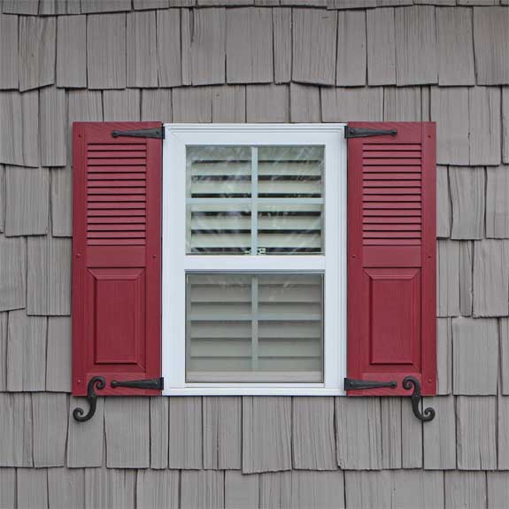 Outdoor vinyl shutters with louvers and raised panels installed on an exterior house window.