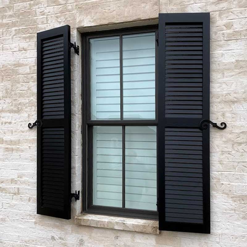 Black louvered shutters installed on a stone window.