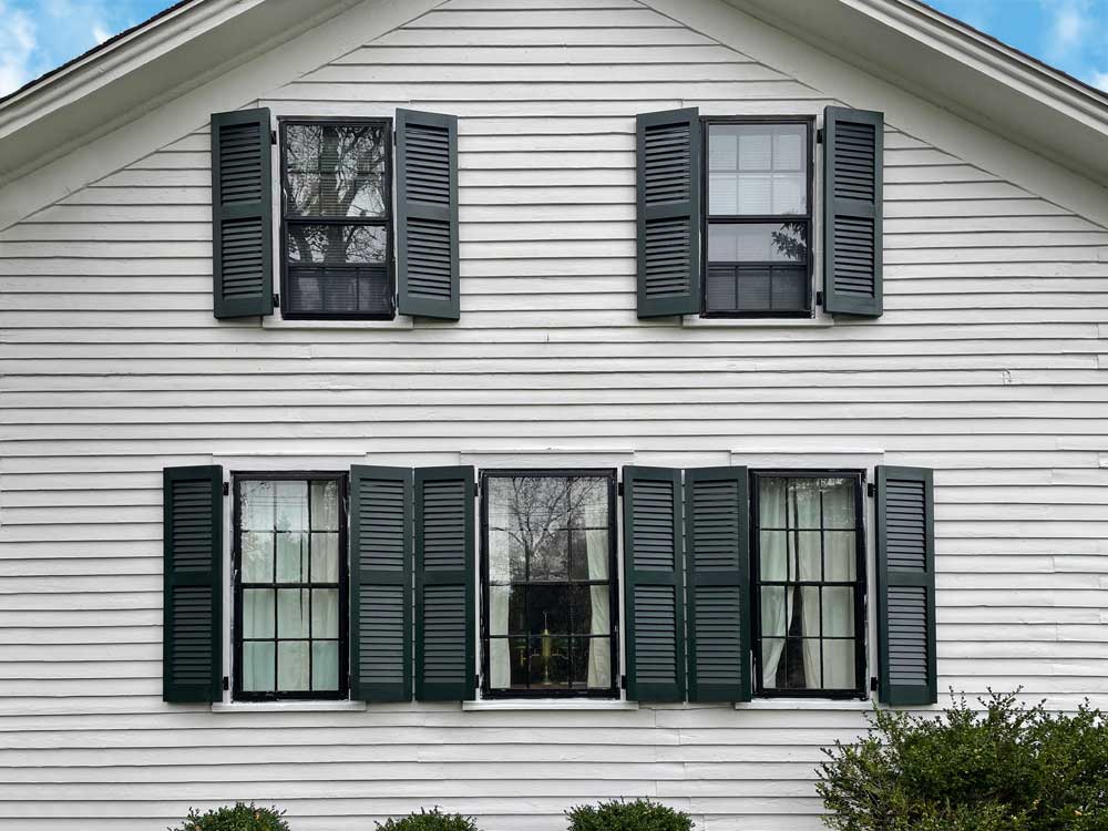 Exterior wood open louvered shutters installed on a white house.