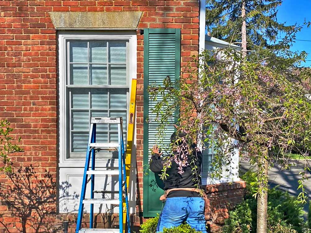 Installing louvered shutters on a brick house.