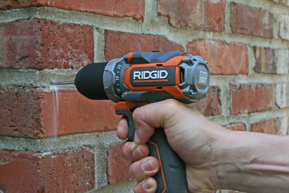 Drill brick with a pilot hole to attach a screw or bolt to hang exterior shutters.