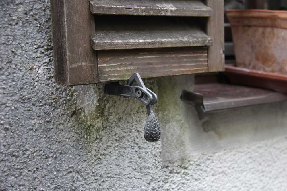 Pine cone shutter tieback lifts to release the shutter from against the building.