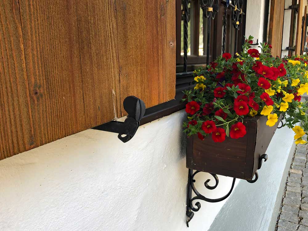 Unique shutter dog restraining a wood shutter agains a house with a flower box.