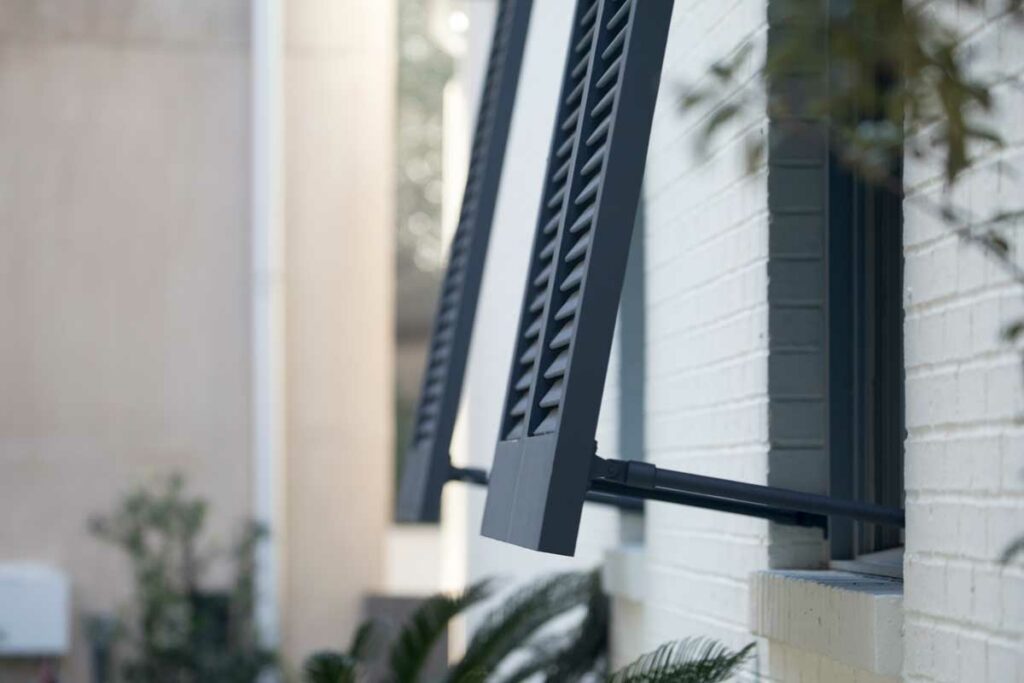 PVC bahama shutters installed on a brick building.