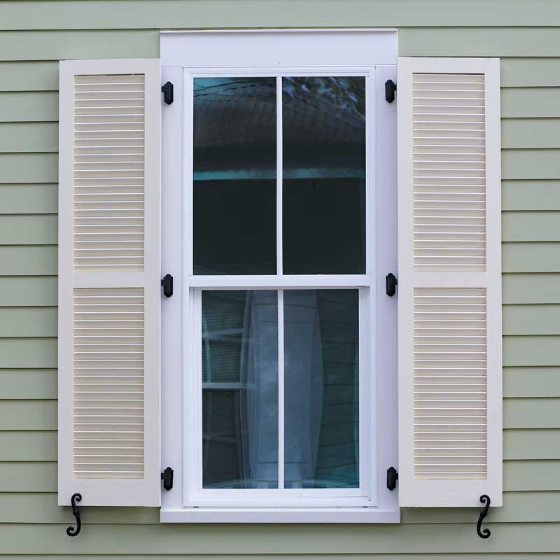 White louvered PVC exterior shutters installed on a window with hinges and shutter dogs.
