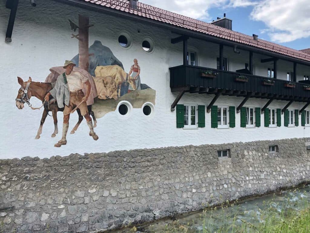 Mural painting with board and batten shutters with cutouts on a German building.