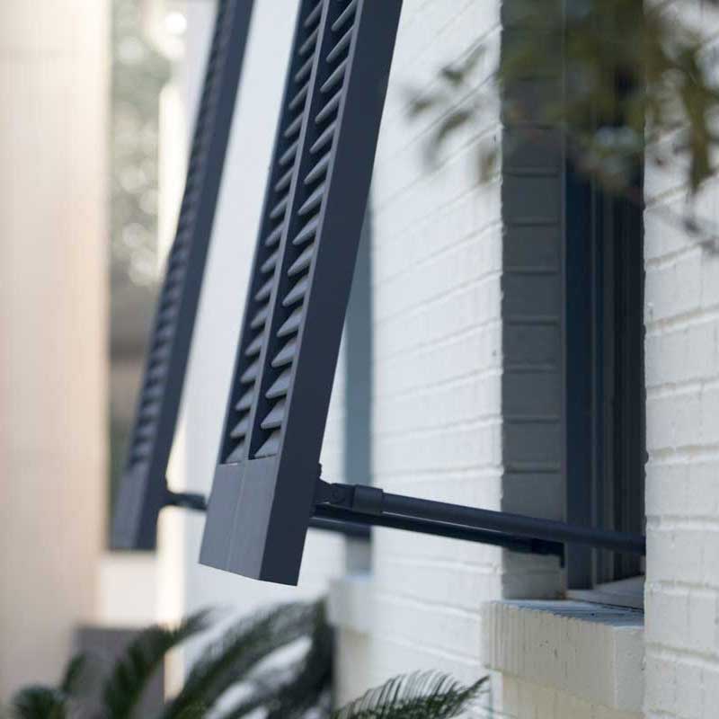 PVC bahama exterior window shutters extended away from a brick house.