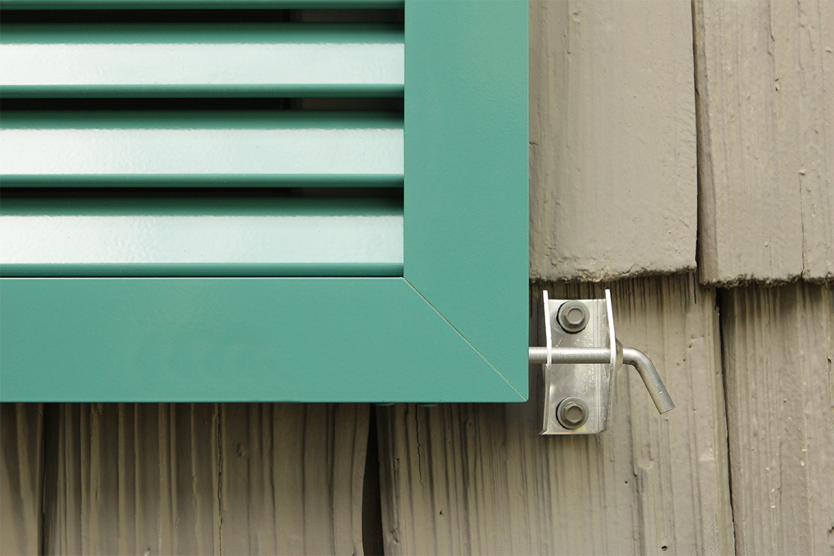 Aluminum bahama shutters locked down with pin through camel bracket to secure from hurricanes.