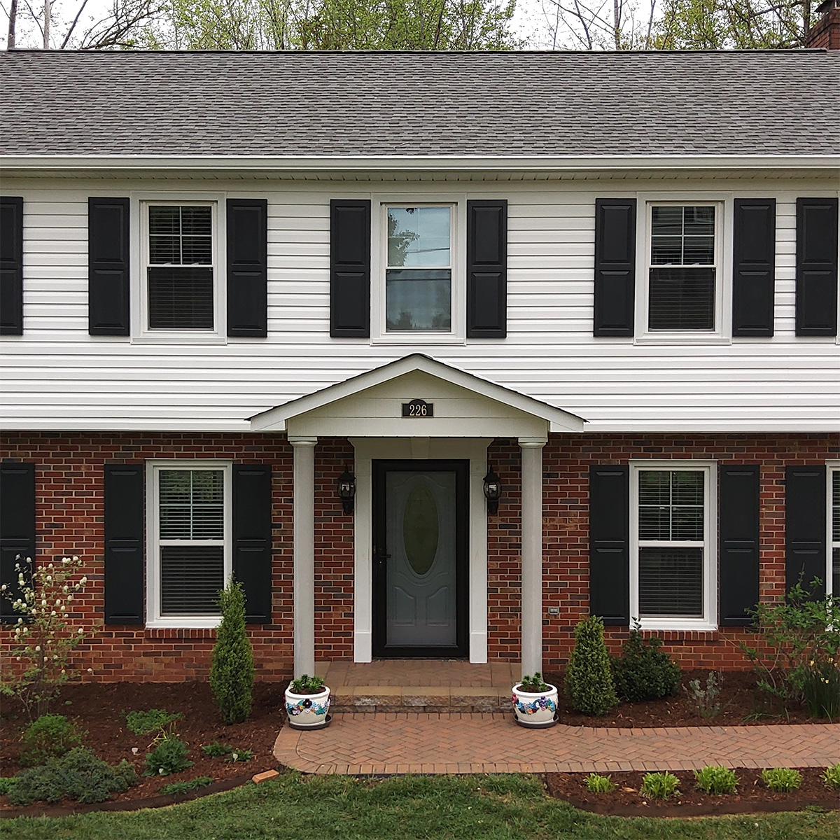 Black wood raised panel exterior shutters installed on brick and siding.